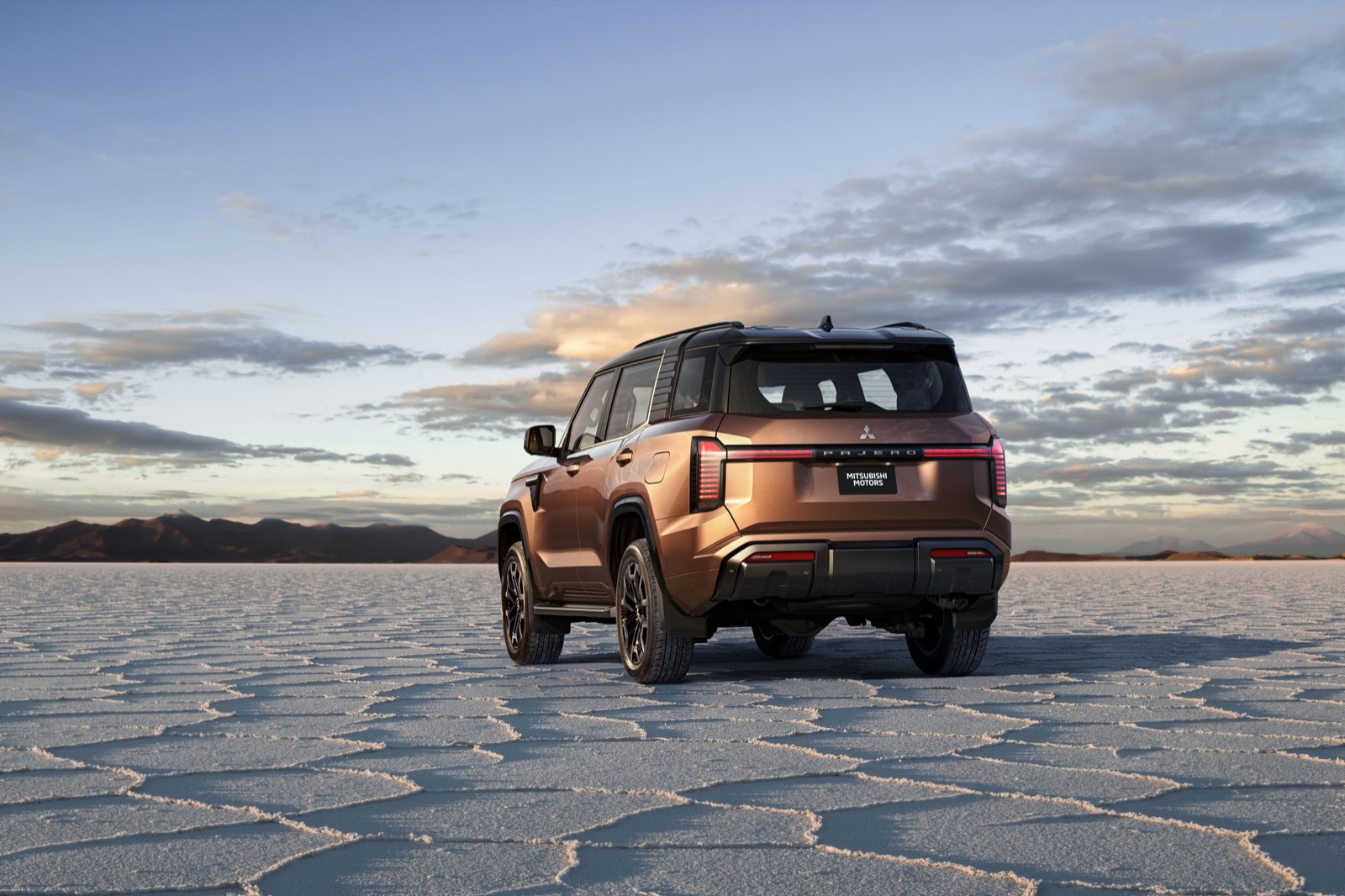 The new Mitsubishi Pajero photographed from the rear three-quarter on a dry salt flat at sunset, showing its squared-off tailgate and vertical rear light bars.